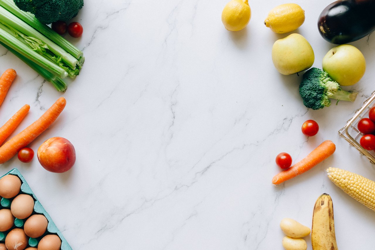 An assortment of fresh fruits and vegetables on a marble background, perfect for healthy lifestyle concepts.